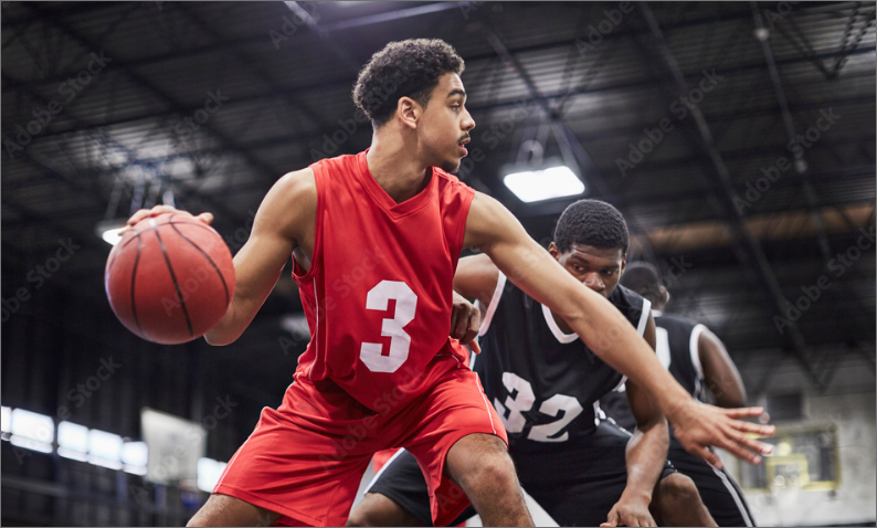 Basketball player in a red jersey with the number 3 dribbling the ball, guarded by two players in black jerseys during a game.